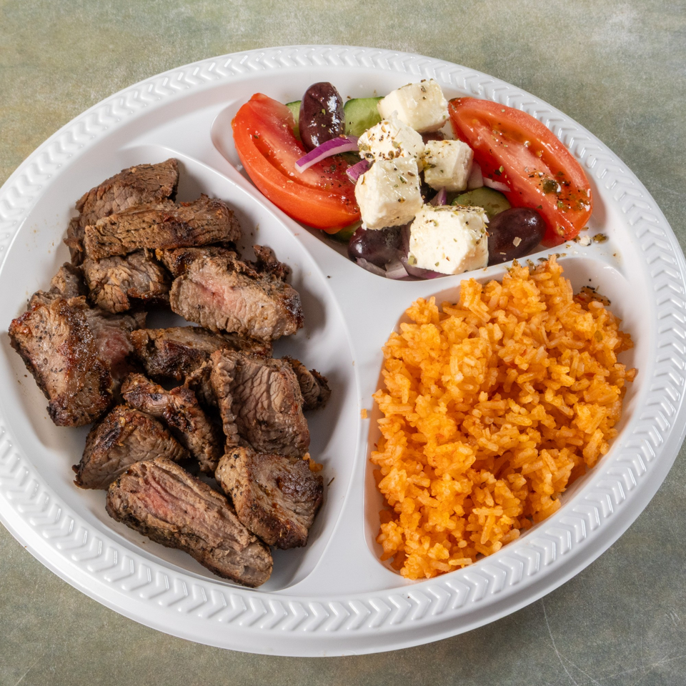 A divided plate with grilled steak, a Greek salad, and orange rice.