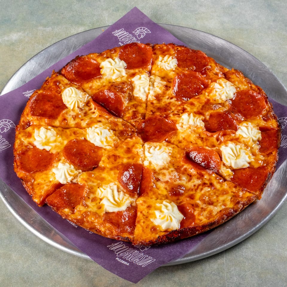 A pepperoni pizza with dollops of white cheese, served on a metal tray with a purple Ambrosia Pizzeria napkin.