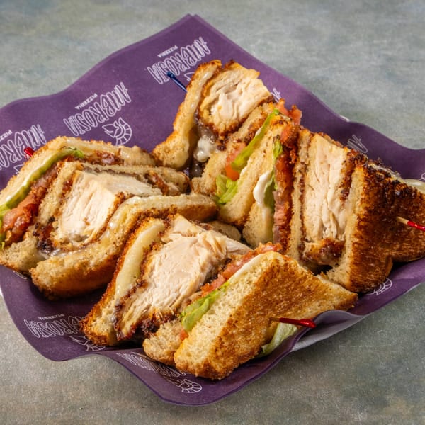 Chicken club sandwiches with lettuce, tomato, and sauce, served on Ambrosia Pizzeria branded paper.
