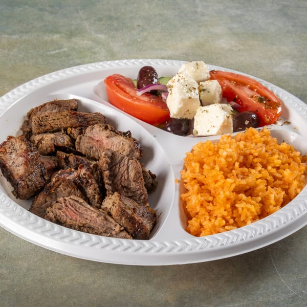 A divided plate with grilled steak, orange rice, and a Greek salad with tomatoes, olives, and feta.